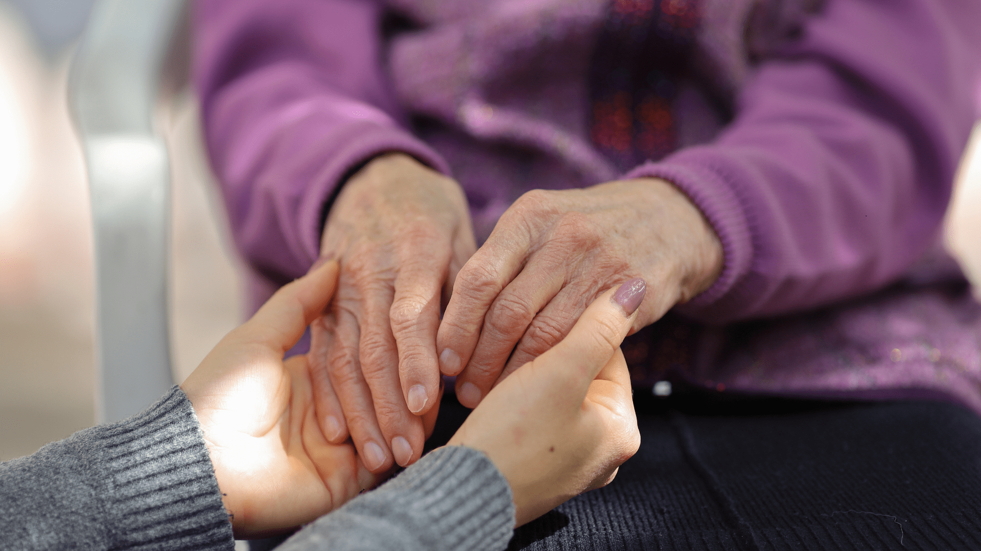 Close-up of a caregiver gently holding an elderly woman's hands in comfort and support
