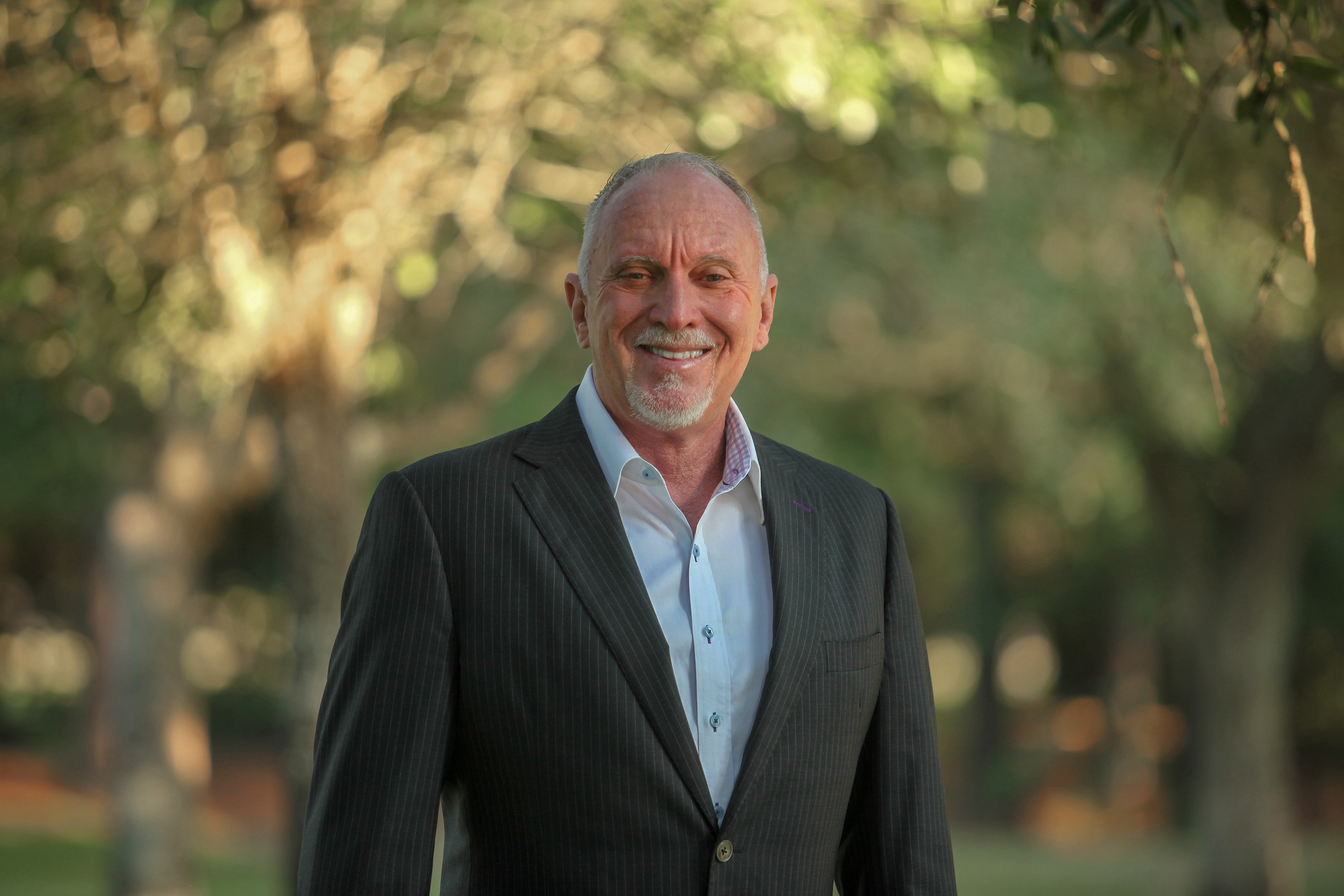 Johnny Burchett smiling outdoors in a suit, relaxed and approachable