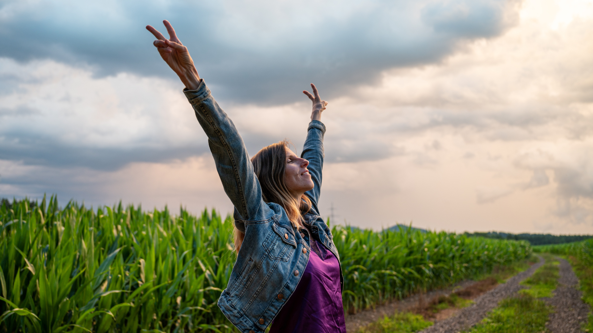 Woman with arms raised toward the sky in a cornfield, smiling in relief and lifted in breakthrough
