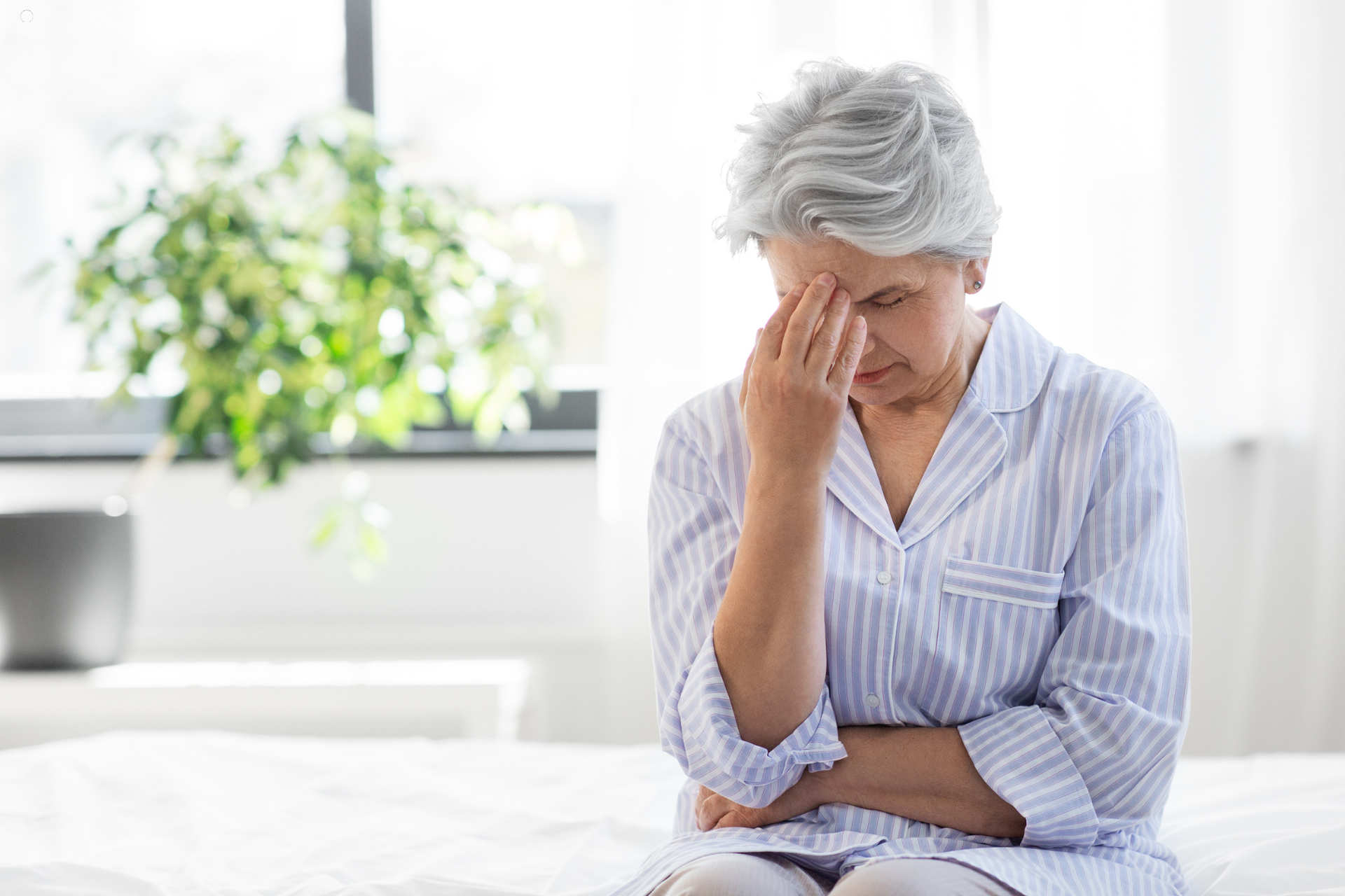 Exhausted older woman sitting on bed, hand to forehead